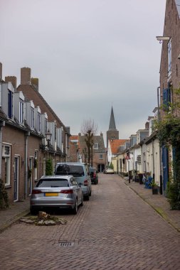 Sessiz bir kaldırım taşı caddesi tarihi tuğla binalar, panjurlar, park edilmiş arabalar ve bulutlu gökyüzünün altında geleneksel sokak lambalarıyla dolu..
