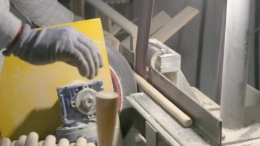 Video, dönen bir makinenin ahşap perdeleri düzleştirdiği ahşap işleme sürecini gösteriyor. Bir işçinin eldivenli eli, atölyedeki talaş ve aletlerle çevrili düzeneği ayarlar..