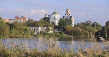 Bereketli bir nehir kenarı manzarası, bir köprü ve tarihi binalar, içinde kubbesi olan bir kilise de var. Sakin su güneşli günün sakin atmosferini yansıtır..