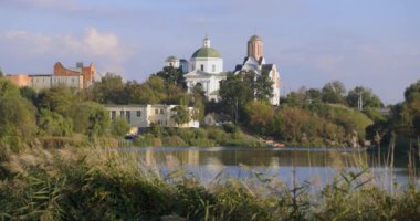 Bereketli bir nehir kenarı manzarası, bir köprü ve tarihi binalar, içinde kubbesi olan bir kilise de var. Sakin su güneşli günün sakin atmosferini yansıtır..