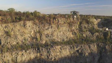 Kuru çalılar ve açık mavi bir gökyüzünün altında yapraksız bir ağaç da dahil olmak üzere seyrek bitki örtüsü olan kayalık bir uçurum. Sahne, sonbaharın başlarında engebeli, doğal bir manzarayı yansıtıyor..