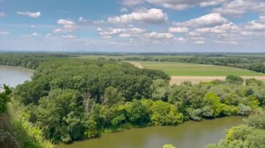 Bereketli mavi gökyüzünün altında tüylü bulutlarla çevrili, bir yamaçta tünemiş antik şato kalıntıları olan sakin bir nehir kenarı manzarası. Tarihle doğanın mükemmel bir karışımı..