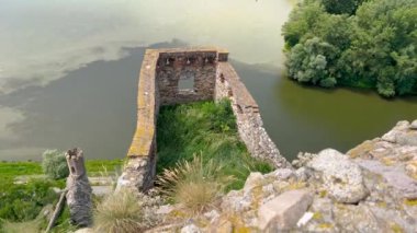 Bereketli mavi gökyüzünün altında tüylü bulutlarla çevrili, bir yamaçta tünemiş antik şato kalıntıları olan sakin bir nehir kenarı manzarası. Tarihle doğanın mükemmel bir karışımı..