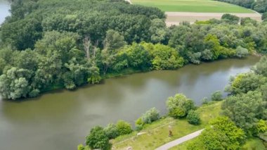 Bereketli yeşil ormanlarla ve açık mavi gökyüzünün altında güneşli bir günde doğanın huzurunu yakalayan bulutlarla çevrili sakin bir nehir manzarası..