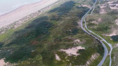 Bereketli yeşillik, kumlu kumullar ve kıyı şeridine paralel uzanan dolambaçlı bir yol olan kıyı manzarası doğanın ve altyapının uyumunu gösteriyor..