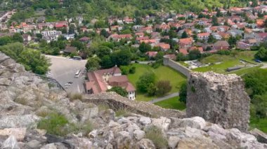 Kırmızı çatılı evleri, yeşil ağaçları ve dolambaçlı yolları olan büyüleyici bir köye bakan bir kalenin enkazından manzara. Barışçıl bir kırsal alan ile harmanlanan tarihi mimariye bir bakış..