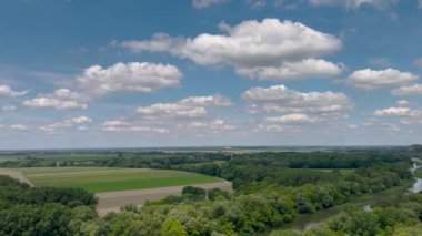 Bereketli yeşil ormanlarla ve açık mavi gökyüzünün altında güneşli bir günde doğanın huzurunu yakalayan bulutlarla çevrili sakin bir nehir manzarası..