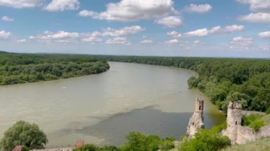Bereketli yeşil ormanlarla ve açık mavi gökyüzünün altında güneşli bir günde doğanın huzurunu yakalayan bulutlarla çevrili sakin bir nehir manzarası..