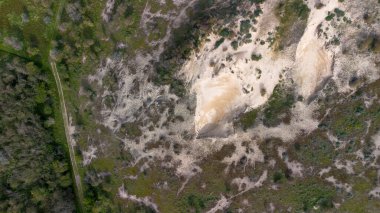 Yeşil bitki örtüsü ve ağaçlarla çevrili kumlu bir bölgenin havadan görünüşü, insansız hava aracından elde edilen çim ve çalılarla doğal bir manzara sergiliyor..
