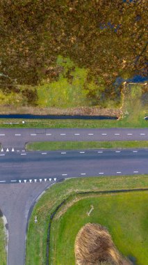 Yeşil çimenler, küçük bir kanal ve sulak arazilerle çevrili düz şeritli bir yolun yer aldığı kırsal bir bölgenin havadan görünüşü. Canlı manzara doğal ve insan unsurlarını sergiliyor..