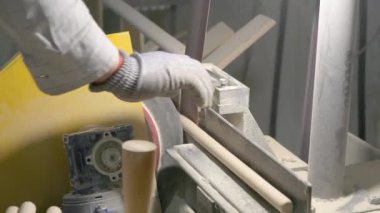 Video, dönen bir makinenin ahşap perdeleri düzleştirdiği ahşap işleme sürecini gösteriyor. Bir işçinin eldivenli eli, atölyedeki talaş ve aletlerle çevrili düzeneği ayarlar..