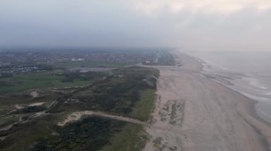 Kumlu bir sahil manzarası, yumuşak okyanus dalgaları ve yemyeşil yemyeşil. Dokunulmamış doğal manzara huzurlu ve resimsel bir ortam yaratır..