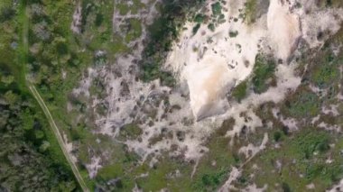 Yeşil bitki örtüsü ve ağaçlarla çevrili kumlu bir bölgenin havadan görünüşü, insansız hava aracından elde edilen çim ve çalılarla doğal bir manzara sergiliyor..