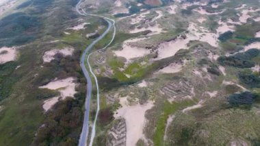 Bereketli yeşillik, kumlu kumullar ve kıyı şeridine paralel uzanan dolambaçlı bir yol olan kıyı manzarası doğanın ve altyapının uyumunu gösteriyor..