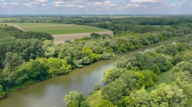Bereketli yeşil ormanlarla ve açık mavi gökyüzünün altında güneşli bir günde doğanın huzurunu yakalayan bulutlarla çevrili sakin bir nehir manzarası..