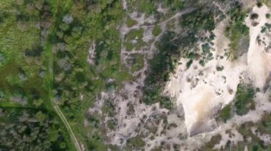 Yeşil bitki örtüsü ve ağaçlarla çevrili kumlu bir bölgenin havadan görünüşü, insansız hava aracından elde edilen çim ve çalılarla doğal bir manzara sergiliyor..