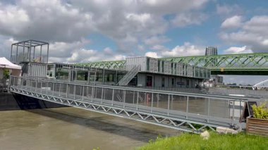 Bratislava, Bratislava Bölgesi, Slovakya Cumhuriyeti - 09.07.2024: Konteynırlardan yapılmış modern bir nehir kenarı yapısı, arka planda yeşil çelik bir köprü, ikincil kemerli bir köprü, bulutlu