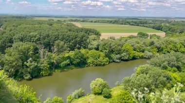 Bereketli yeşil ormanlarla ve açık mavi gökyüzünün altında güneşli bir günde doğanın huzurunu yakalayan bulutlarla çevrili sakin bir nehir manzarası..