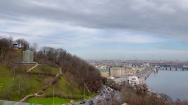 Nehir, köprüler ve modern binaları olan panoramik bir şehir manzarası. Gökyüzü parçalı bulutlu ve yol boyunca trafik hareket ediyor. Sakin nehir ufku yansıtıyor, şehir manzarası yaratıyor..