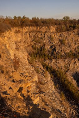 Sert dokuları olan kayalık kayalık, altın güneş ışığı ve seyrek bitki örtüsü. Engebeli arazi, etrafa saçılmış kuru bitkiler ve topraksı tonlarla doğal aşınmayı vurguluyor..