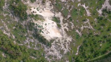 Yeşil bitki örtüsü ve ağaçlarla çevrili kumlu bir bölgenin havadan görünüşü, insansız hava aracından elde edilen çim ve çalılarla doğal bir manzara sergiliyor..