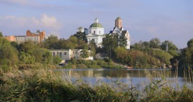 Bereketli bir nehir kenarı manzarası, bir köprü ve tarihi binalar, içinde kubbesi olan bir kilise de var. Sakin su güneşli günün sakin atmosferini yansıtır..
