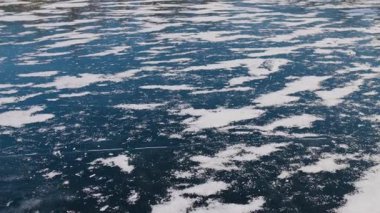 Buz tabakası kısmen karla kaplı donmuş bir göl. Koyu mavi yüzey dağınık beyaz yamalarla çelişiyor ve desenli bir kış manzarası yaratıyor. Buzdaki çatlaklar göze çarpmıyor..