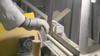Video, dönen bir makinenin ahşap perdeleri düzleştirdiği ahşap işleme sürecini gösteriyor. Bir işçinin eldivenli eli, atölyedeki talaş ve aletlerle çevrili düzeneği ayarlar..