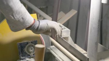 Video, dönen bir makinenin ahşap perdeleri düzleştirdiği ahşap işleme sürecini gösteriyor. Bir işçinin eldivenli eli, atölyedeki talaş ve aletlerle çevrili düzeneği ayarlar..