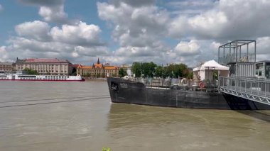 Bratislava, Bratislava Bölgesi, Slovakya Cumhuriyeti - 09.07.2024: Bir tepede Bratislava Kalesi, nehirde bir yolcu gemisi, St. Martin Katedrali 'nde sakin bir nehir manzarası gösteren bir video