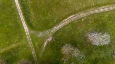 Dağılmış ağaçlar ve açık yeşil alanlarla çevrili, kesişen toprak yollarla dolu çimenli bir arazinin havadan görünüşü, sakin ve doğal bir doğa manzarası yakalıyor..