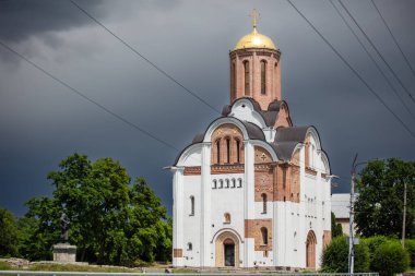 Resimli, yemyeşil bir kasaba ve arka planda altın kubbeli kiliseler. Dramatik gökyüzü kontrastı ekliyor, sakin ama dengesiz bir atmosfer yaratıyor..