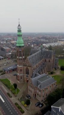 Sessiz bir kasaba, yollar ve bulutlu bir gökyüzünün altındaki uzak tarlalarla çevrili yeşil kulesi olan yüksek bir kilise kulesinin havadan görünüşü. Mimari klasik ve detaylı..