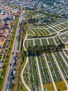 Simetrik mezar sıraları, merkezi bir yuvarlak bina ve çevreleyen yeşilliklerle dolu bir mezarlığın havadan görünüşü. Yollar ve ağaçlar yukarıdan düzenli ve barışçıl bir düzen oluşturur..