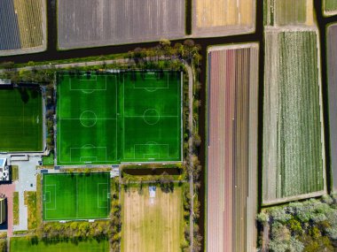 Çiçek açan lale tarlaları ve dar kanallarla çevrili, spor altyapısını renkli Hollanda tarım arazisiyle harmanlayan birden fazla futbol sahasının yukarıdan aşağıya havadan görünüşü.