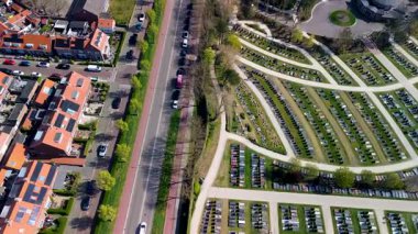 Yuvarlak yolları ve mezar taşlarıyla çevrili, ağaçlarla çevrili ve açık mavi gökyüzünün altındaki yerleşim alanına komşu büyük, düzenli bir mezarlığın havadan görünüşü..