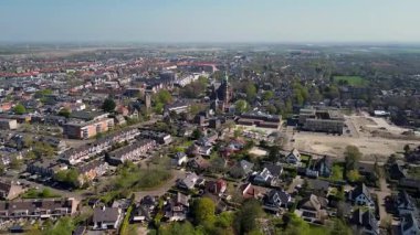 Merkezinde konut evleri, yeşil ağaçlar ve açık mavi bir bahar gününde açık mavi gökyüzü ile çevrili önemli bir kilisenin bulunduğu bir Hollanda kasabasının havadan görünüşü. Huzurlu ve büyüleyici bir atmosfer.