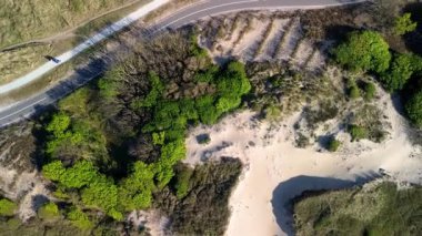 Yeşil tepeleri ve kumlu kum tepelerini kesen tepeden aşağı sarmal hava manzarası, küçük bir açıklık ve park edilmiş bisikletle doğal manzara arasında görülebilir..