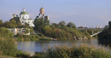 Güneş ışığı, sakin bir gölün kenarında hafifçe sallanıyor, altın renkleri, etraflarındaki yeşillikle çelişiyor, yumuşak, sıcak bir ışığın altında sakin ve huzurlu bir doğal manzara yaratıyor..