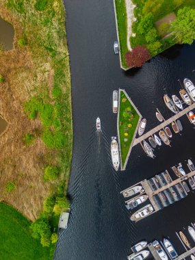Ahşap rıhtımlar boyunca kenetlenmiş bir marina manzarası, yeşil parklar ve doğal otlaklarla çevrili dar bir su yolunda seyreden bir tekne..