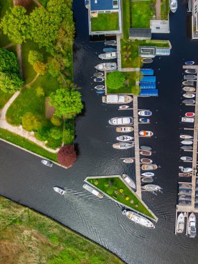 Ahşap rıhtımlar boyunca kenetlenmiş bir marina manzarası, yeşil parklar ve doğal otlaklarla çevrili dar bir su yolunda seyreden bir tekne..