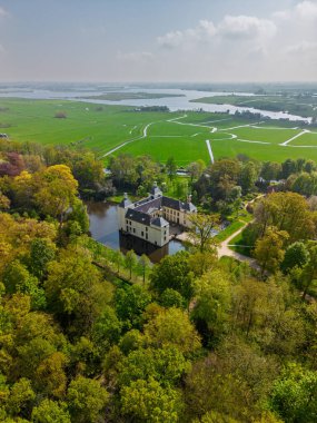 Uçsuz bucaksız yeşil tarlaları, dolambaçlı su yolları ve Hollanda 'nın düz kırsalında parçalı bulutlu bir gökyüzünün altında uzanan bir nehirle çevrili tarihi bir şatonun havadan görünüşü..