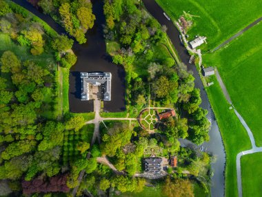Uçsuz bucaksız yeşil tarlaları, dolambaçlı su yolları ve Hollanda 'nın düz kırsalında parçalı bulutlu bir gökyüzünün altında uzanan bir nehirle çevrili tarihi bir şatonun havadan görünüşü..