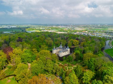 Uçsuz bucaksız yeşil tarlaları, dolambaçlı su yolları ve Hollanda 'nın düz kırsalında parçalı bulutlu bir gökyüzünün altında uzanan bir nehirle çevrili tarihi bir şatonun havadan görünüşü..