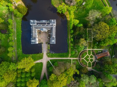 Uçsuz bucaksız yeşil tarlaları, dolambaçlı su yolları ve Hollanda 'nın düz kırsalında parçalı bulutlu bir gökyüzünün altında uzanan bir nehirle çevrili tarihi bir şatonun havadan görünüşü..