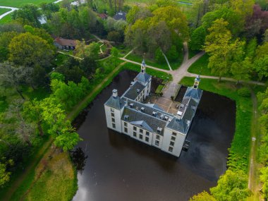 Uçsuz bucaksız yeşil tarlaları, dolambaçlı su yolları ve Hollanda 'nın düz kırsalında parçalı bulutlu bir gökyüzünün altında uzanan bir nehirle çevrili tarihi bir şatonun havadan görünüşü..