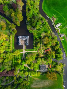 Uçsuz bucaksız yeşil tarlaları, dolambaçlı su yolları ve Hollanda 'nın düz kırsalında parçalı bulutlu bir gökyüzünün altında uzanan bir nehirle çevrili tarihi bir şatonun havadan görünüşü..