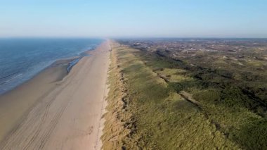 Yumuşak dalgaların kumlu sahille buluştuğu sahilin havadan görünüşü. İnsanlar kuma dağılmış durumda, bazıları kumdan kaleler yapıyor, diğerleri güneşli günün tadını çıkarıyor..