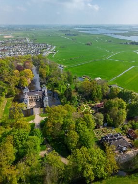 Uçsuz bucaksız yeşil tarlaları, dolambaçlı su yolları ve Hollanda 'nın düz kırsalında parçalı bulutlu bir gökyüzünün altında uzanan bir nehirle çevrili tarihi bir şatonun havadan görünüşü..