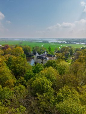 Uçsuz bucaksız yeşil tarlaları, dolambaçlı su yolları ve Hollanda 'nın düz kırsalında parçalı bulutlu bir gökyüzünün altında uzanan bir nehirle çevrili tarihi bir şatonun havadan görünüşü..